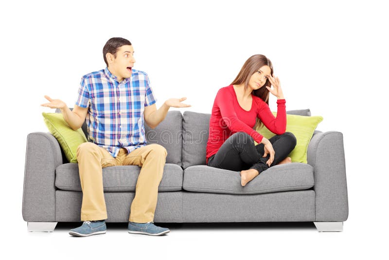 Pares heterosexuales jovenes que se sientan en un sofá durante una discusión