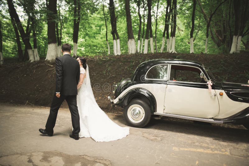 Pares, hombre feliz y esposa del recién casado besándose cerca del coche retro elegante imagen de archivo Pares, hombre feliz y esposa del recién casado besándose cerca del coche retro elegante imagen de archivo