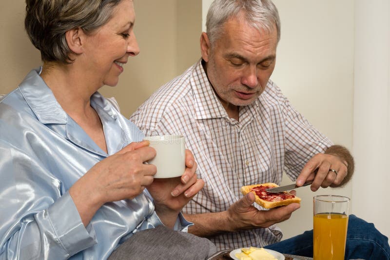 Pares idosos que comem o café da manhã romântico na cama fotos de stock Pares idosos que comem o café da manhã romântico na cama fotos de stock