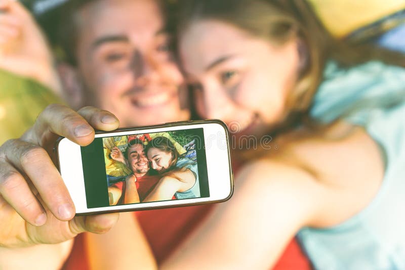 Pares jovenes de los amantes que toman que mienten en la hierba que toma un selfie con el tel?fono m?vil imágenes de archivo libres de regalías Pares jovenes de los amantes que toman que mienten en la hierba que toma un selfie con el tel?fono m?vil imágenes de archivo libres de regalías