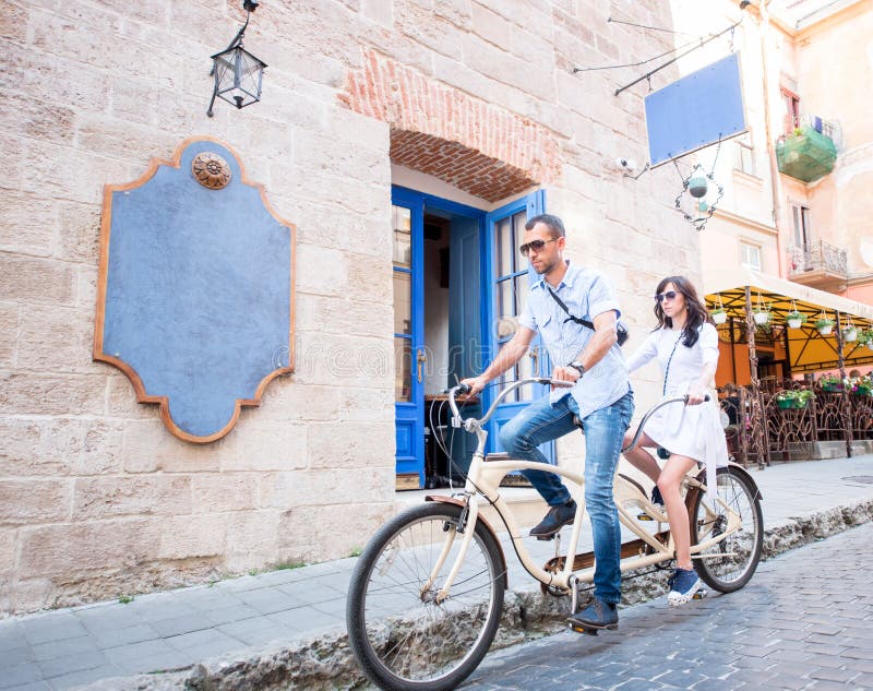 Pares jovenes en la bicicleta en tándem en la ciudad de la calle imágenes de archivo libres de regalías Pares jovenes en la bicicleta en tándem en la ciudad de la calle imágenes de archivo libres de regalías