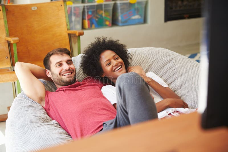 Pares jovenes en los pijamas que miran la televisión junto imagenes de archivo Pares jovenes en los pijamas que miran la televisión junto imagenes de archivo
