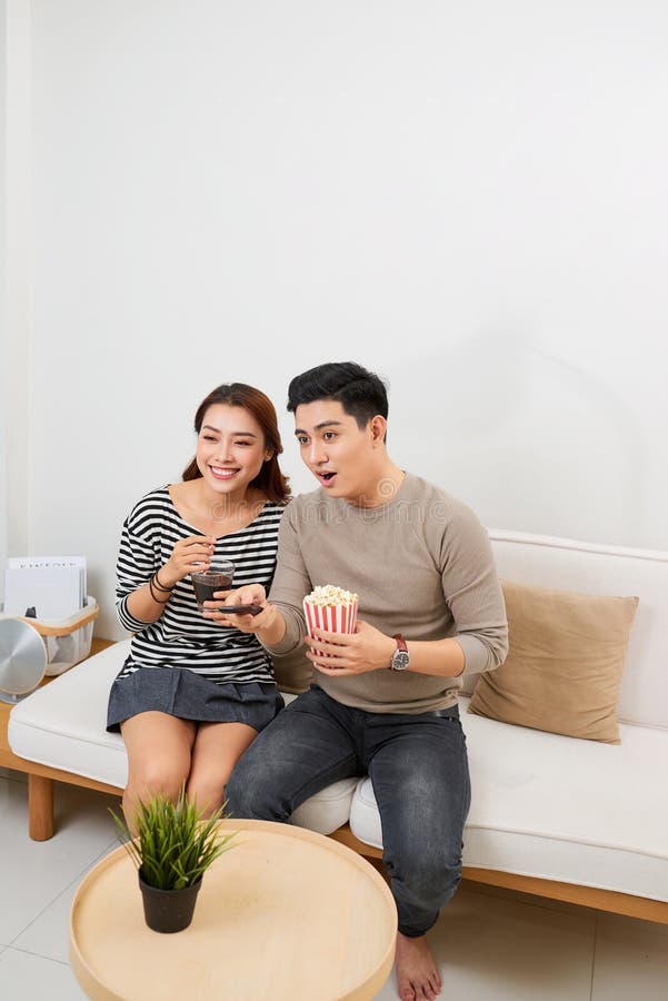 Pares jovenes felices que mienten en el sof? en casa con las palomitas que ven la TV imágenes de archivo libres de regalías Pares jovenes felices que mienten en el sof? en casa con las palomitas que ven la TV imágenes de archivo libres de regalías