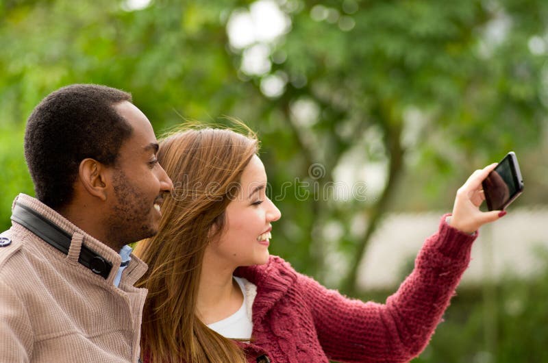 Pares jovenes interraciales felices hermosos y sonrientes en el parl que toma un selfie fotos de archivo libres de regalías Pares jovenes interraciales felices hermosos y sonrientes en el parl que toma un selfie fotos de archivo libres de regalías