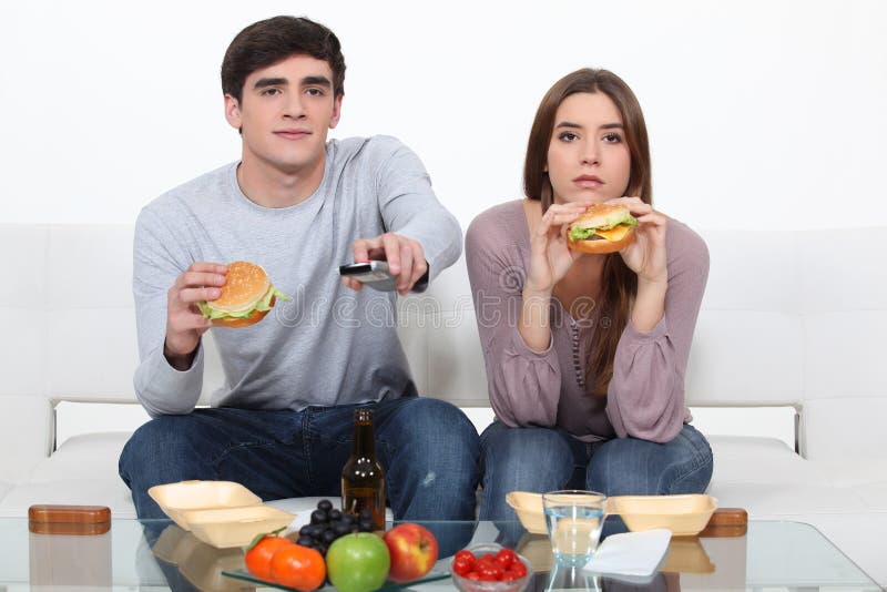 Pares jovenes que comen las hamburguesas fotografía de archivo libre de regalías Pares jovenes que comen las hamburguesas fotografía de archivo libre de regalías