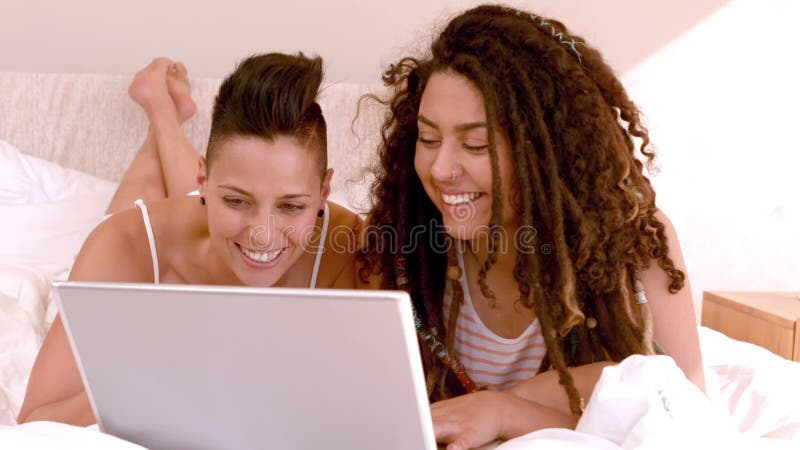 Pares lesbianos felices usando el ordenador portátil en cama