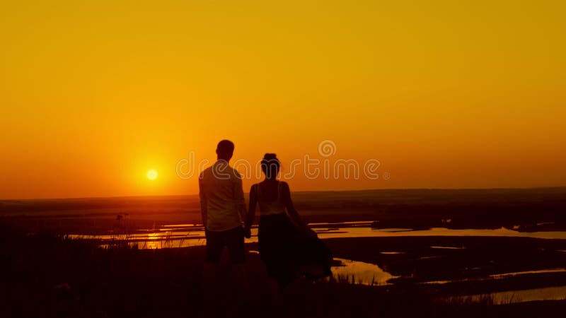 Pares loving no por do sol - o homem novo e a menina bonita estão no prado do verão e na vista para expor-se ao sol, para mostrar