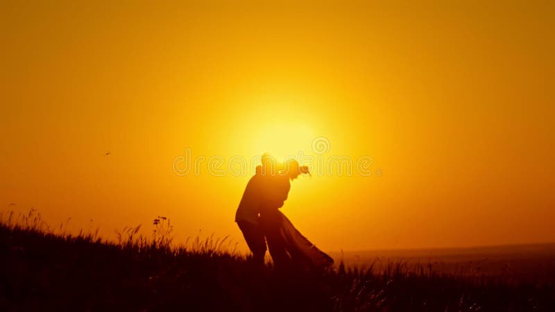 Pares loving - o homem novo corajoso e a menina bonita estão no prado do verão no por do sol e têm abraços e beijo, silhueta