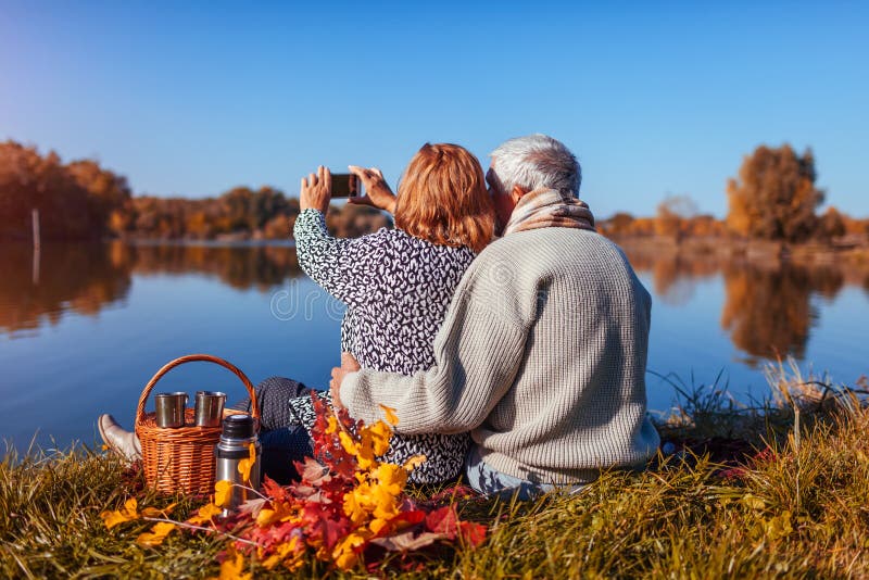Pares mayores que toman el selfie mientras que teniendo comida campestre por el lago del oto? o Hombre feliz y mujer que disfrutan imagenes de archivo