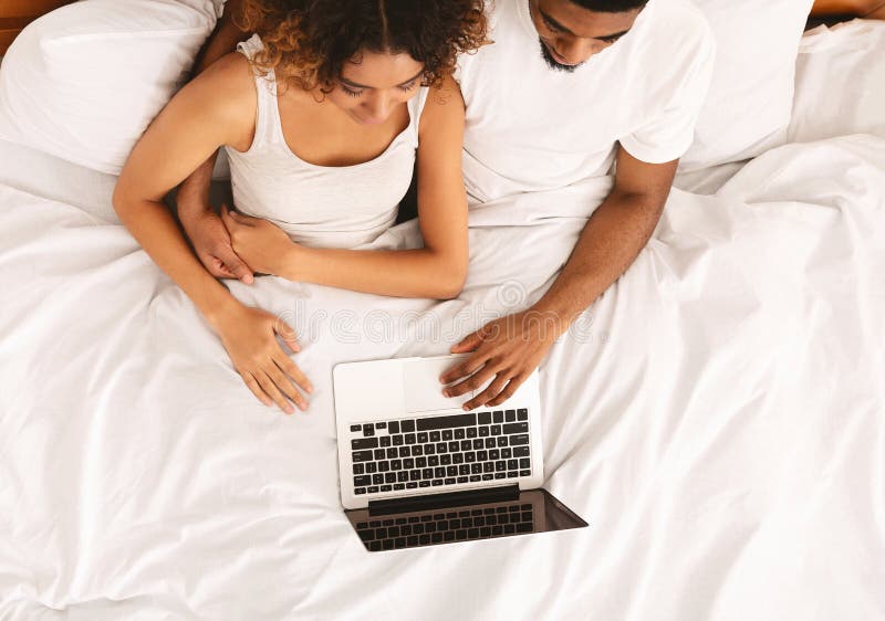 Pares negros jovenes que mienten en cama y que usan el ordenador port?til fotos de archivo libres de regalías Pares negros jovenes que mienten en cama y que usan el ordenador port?til fotos de archivo libres de regalías