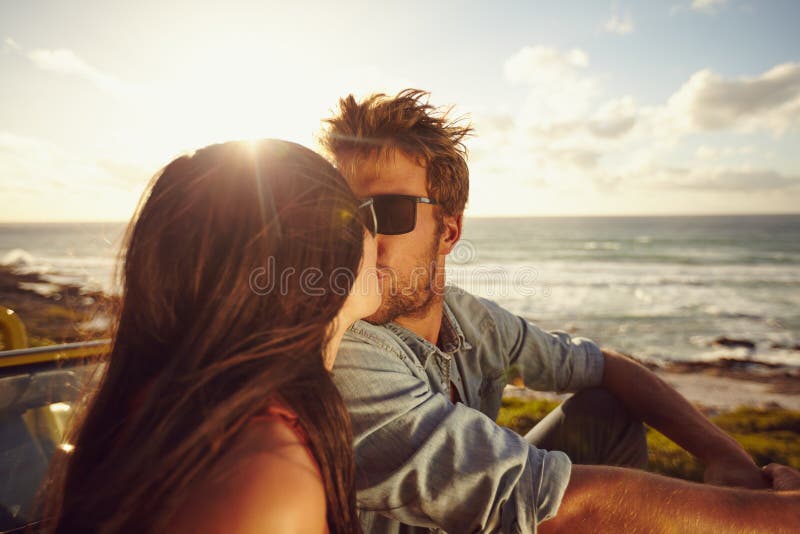 Pares novos afetuosos que beijam na praia