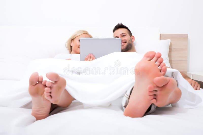 Pares novos bonitos usando um PC da tabuleta na cama fotografia de stock royalty free Pares novos bonitos usando um PC da tabuleta na cama fotografia de stock royalty free