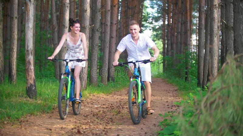 Pares novos caucasianos que têm o divertimento que aprecia a ciclagem na floresta