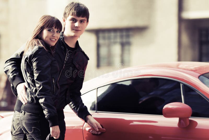 Pares novos felizes ao lado do carro de esportes fotografia de stock Pares novos felizes ao lado do carro de esportes fotografia de stock