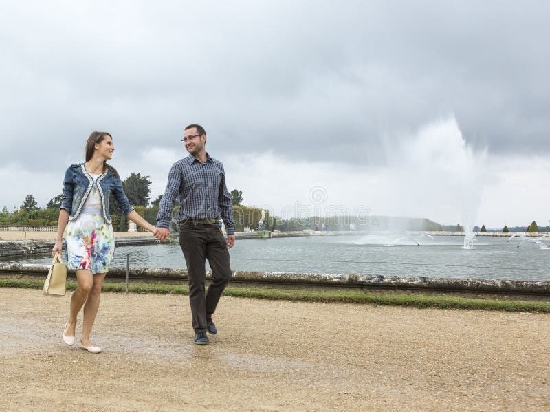 Pares novos felizes que andam em um jardim francês fotografia de stock Pares novos felizes que andam em um jardim francês fotografia de stock
