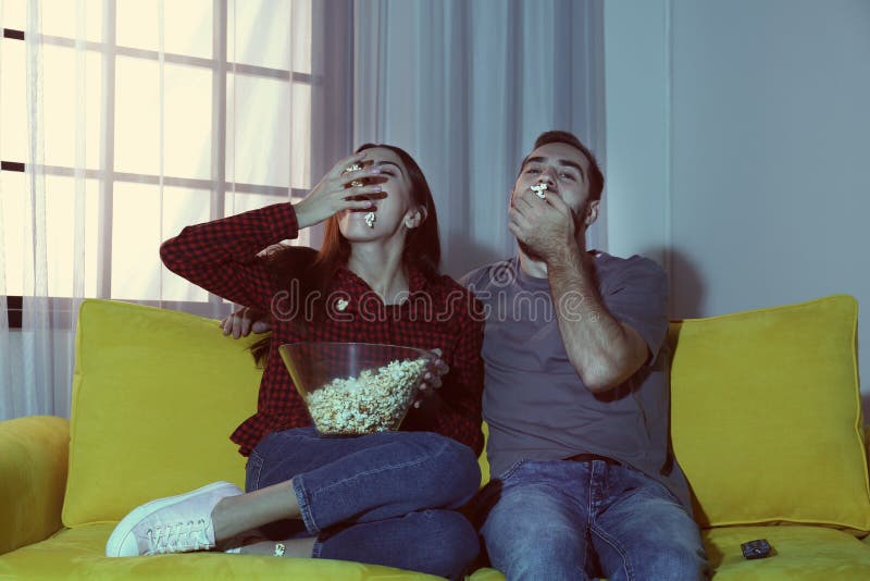 Pares novos felizes que comem a pipoca ao olhar a tevê fotos de stock Pares novos felizes que comem a pipoca ao olhar a tevê fotos de stock
