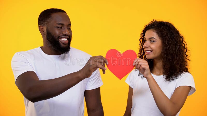 Pares novos felizes que guardam o coração de papel vermelho e o amor e o cuidado sorrindo, verdadeiros foto de stock royalty free Pares novos felizes que guardam o coração de papel vermelho e o amor e o cuidado sorrindo, verdadeiros foto de stock royalty free