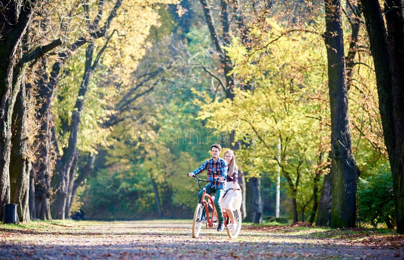 Pares novos, homem considerável e mulher atrativa na bicicleta em tandem no parque ou na floresta ensolarada do verão foto de stock Pares novos, homem considerável e mulher atrativa na bicicleta em tandem no parque ou na floresta ensolarada do verão foto de stock