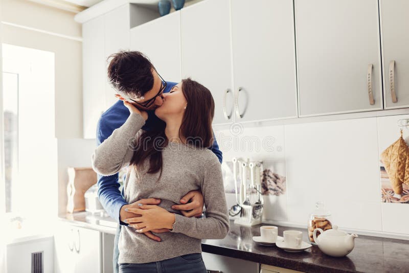 Pares novos na cozinha que abraça e que beija imagens de stock Pares novos na cozinha que abraça e que beija imagens de stock