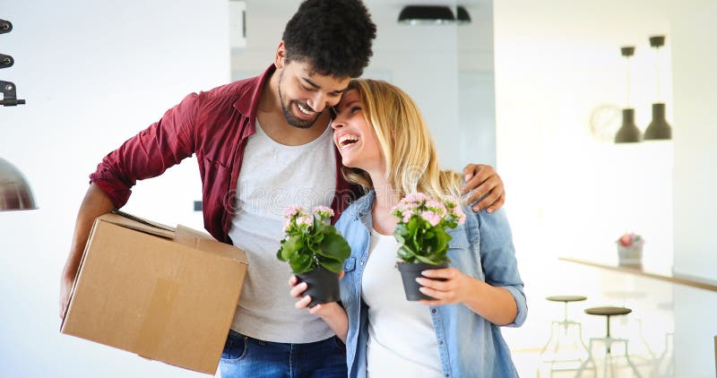 Pares novos que desembalam caixas de cartão na casa nova que move-se no conceito fotografia de stock Pares novos que desembalam caixas de cartão na casa nova que move-se no conceito fotografia de stock