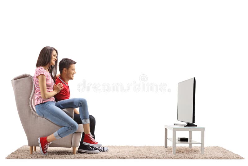 Pares novos que sentam-se em uma poltrona e em uma televisão de observação fotografia de stock Pares novos que sentam-se em uma poltrona e em uma televisão de observação fotografia de stock