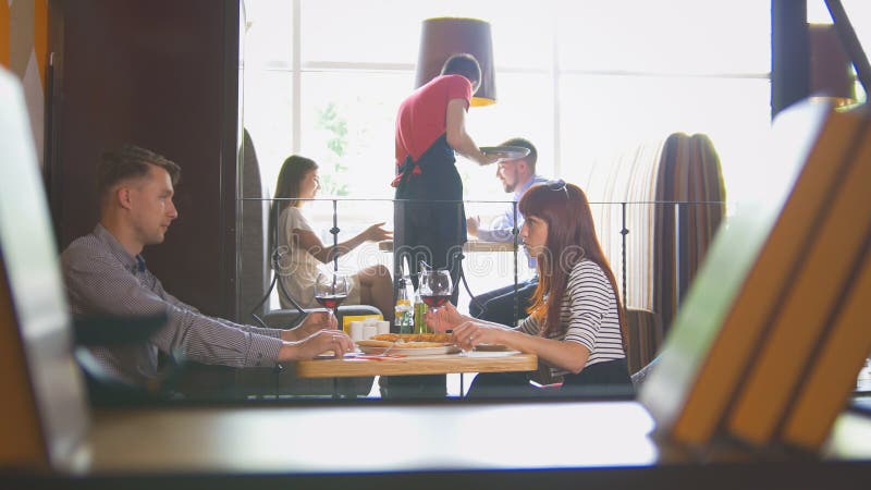 Pares novos que sentam-se no vinho de fala e bebendo do restaurante imagem de stock Pares novos que sentam-se no vinho de fala e bebendo do restaurante imagem de stock