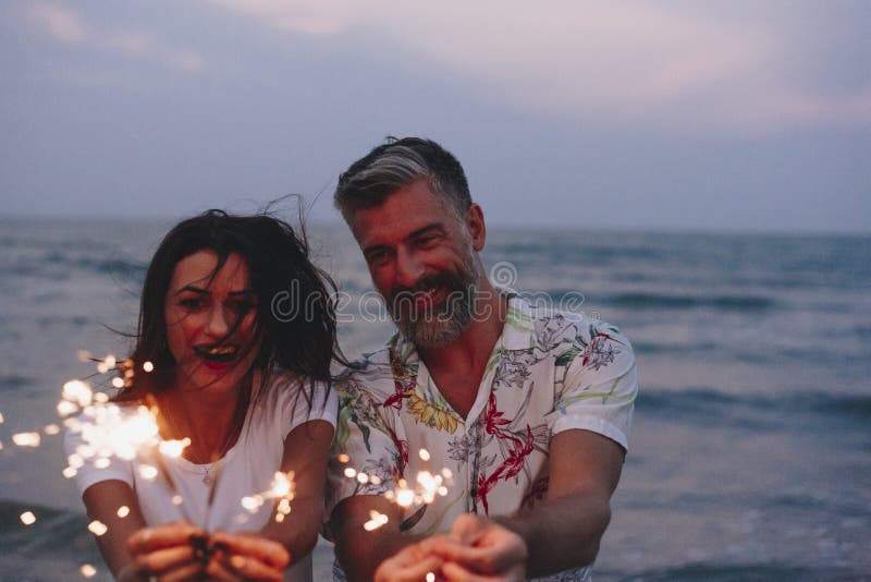 Pares que celebran con las bengalas en la playa imágenes de archivo libres de regalías Pares que celebran con las bengalas en la playa imágenes de archivo libres de regalías
