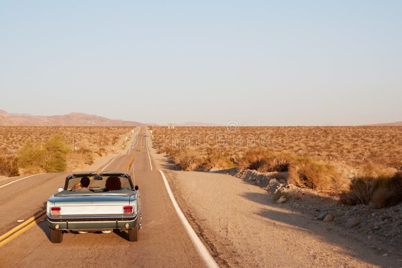 Pares que conduzem o carro convertível na estrada do deserto, vista traseira