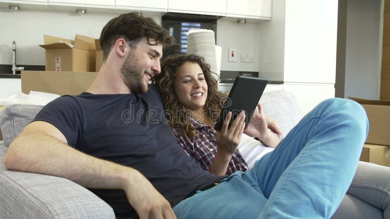 Pares que relaxam na casa nova de Sofa With Digital Tablet In