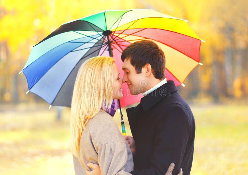 Pares que se besan románticos del retrato en amor con el paraguas colorido junto en el día soleado caliente sobre las hojas amari fotos de archivo libres de regalías Pares que se besan románticos del retrato en amor con el paraguas colorido junto en el día soleado caliente sobre las hojas amari fotos de archivo libres de regalías