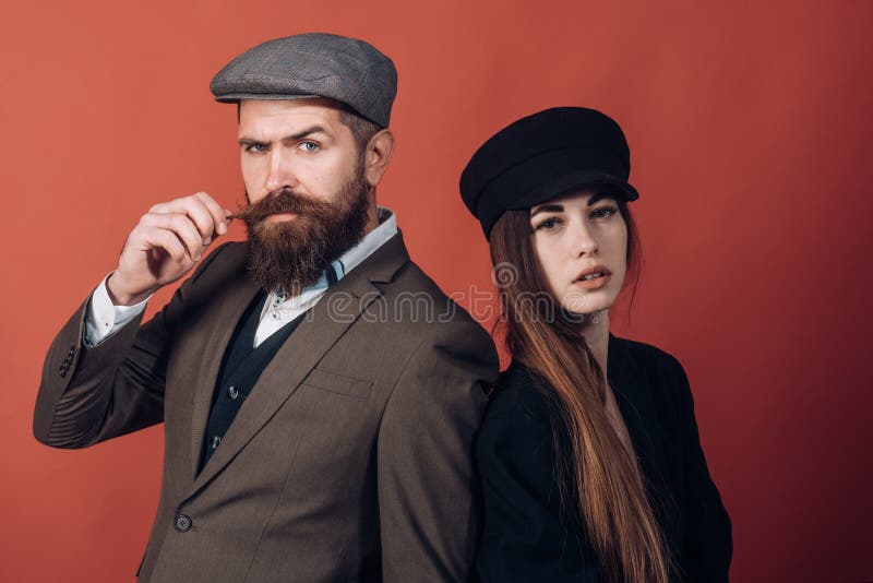 Vintage retro couple on red wall. Old style hat on bearded men and black fashion cap on beauty woman. Vintage retro couple on red wall. Old style hat on bearded men and black fashion cap on beauty woman