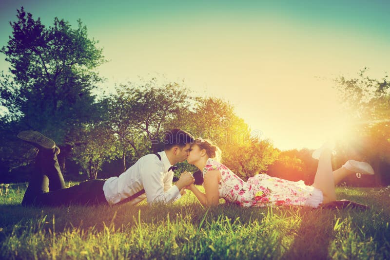 Pares románticos en el amor que se besa mientras que miente en hierba vendimia imagenes de archivo Pares románticos en el amor que se besa mientras que miente en hierba vendimia imagenes de archivo
