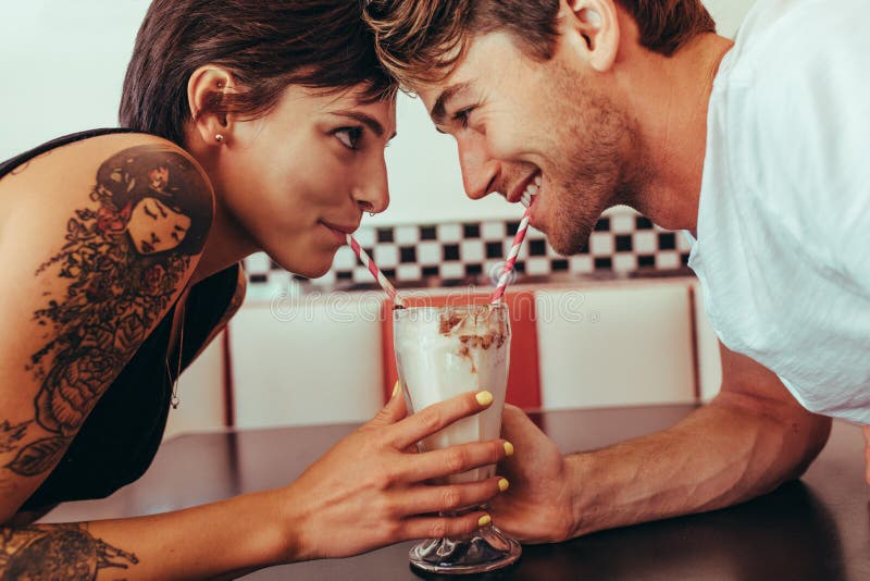 Pares románticos que comparten el batido de leche usando la paja del mismo gl imagen de archivo libre de regalías Pares románticos que comparten el batido de leche usando la paja del mismo gl imagen de archivo libre de regalías