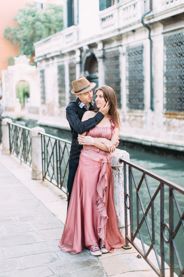 Pares românticos que beijam em Veneza, Itália Menina no vestido cor-de-rosa e no menino no chapéu e na roupa preta que andam ruas fotografia de stock royalty free Pares românticos que beijam em Veneza, Itália Menina no vestido cor-de-rosa e no menino no chapéu e na roupa preta que andam ruas fotografia de stock royalty free