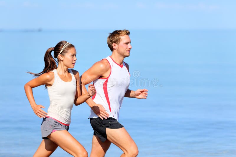 Pares running que movimentam-se na praia