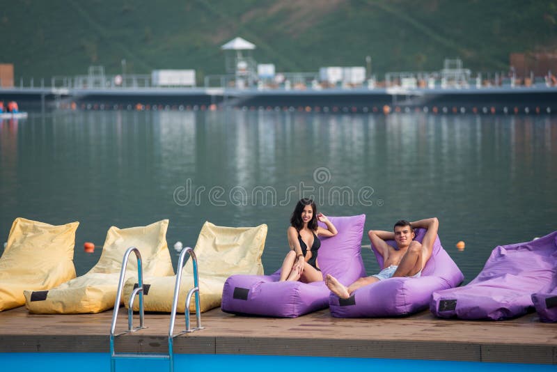 Pares 'sexy' novos em vadios amortecidos pela piscina e lago no fundo fotografia de stock Pares 'sexy' novos em vadios amortecidos pela piscina e lago no fundo fotografia de stock