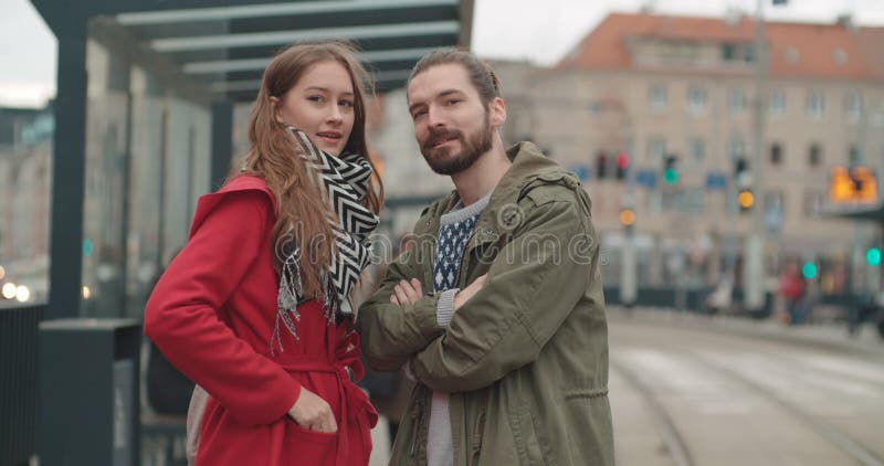 Pares sonrientes que miran ausentes mientras que espera la parada de la tranvía en una ciudad