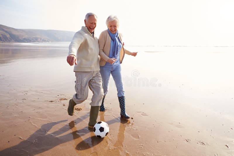 Pares superiores que jogam o futebol na praia do inverno fotos de stock royalty free Pares superiores que jogam o futebol na praia do inverno fotos de stock royalty free