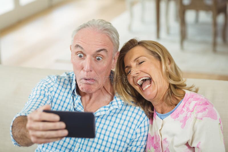 Pares superiores que tomam um selfie no telefone celular na sala de visitas foto de stock Pares superiores que tomam um selfie no telefone celular na sala de visitas foto de stock