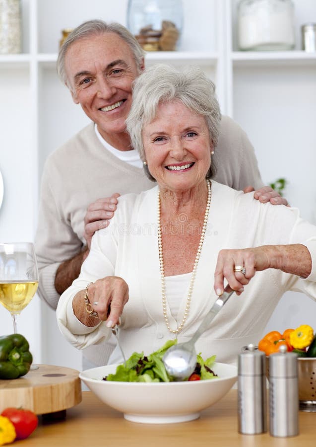 Pares sênior felizes que comem uma salada na cozinha fotografia de stock Pares sênior felizes que comem uma salada na cozinha fotografia de stock