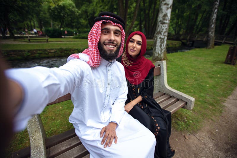 Pares árabes bonitos novos ocasionais e hijab, Abaya, tomando um selfie no gramado no parque do verão fotos de stock Pares árabes bonitos novos ocasionais e hijab, Abaya, tomando um selfie no gramado no parque do verão fotos de stock