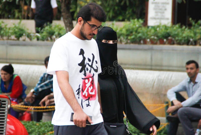 Pares árabes: un hombre joven con vidrios y una barba está caminando con una mujer vestida en un burka negro foto de archivo libre de regalías Pares árabes: un hombre joven con vidrios y una barba está caminando con una mujer vestida en un burka negro foto de archivo libre de regalías