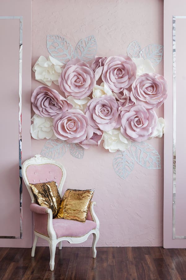 Parete rosa con le rose rosa, accanto ad una sedia d'annata rosa con due cuscini dorati