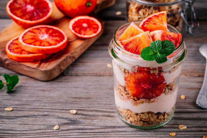 Parfait de vidro do iogurte do frasco do café da manhã saudável com granola caseiro e laranja pigmentada em um fundo de madeira imagens de stock Parfait de vidro do iogurte do frasco do café da manhã saudável com granola caseiro e laranja pigmentada em um fundo de madeira imagens de stock
