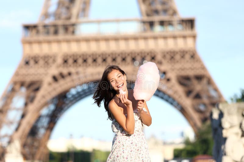 Paris Eiffel Tower woman smiling happy and cheerful eating cotton candy in front of Eiffel Tower in Paris, France. Cute Asian / Caucasian girl.