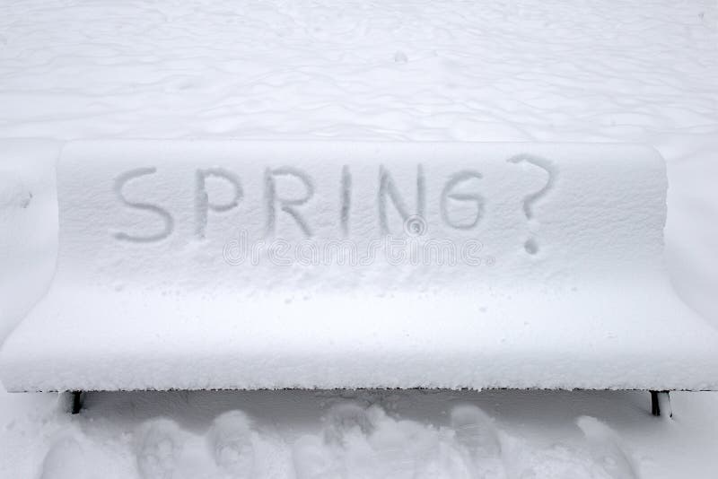 Park bench covered with snow and written Spring in English
