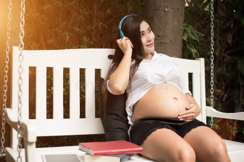 Parkerar koppla av och lyssnande musik för asiatisk ung gravid kvinna på gunga in trädgården med böcker Folk- och underh?llningbe royaltyfri fotografi Parkerar koppla av och lyssnande musik för asiatisk ung gravid kvinna på gunga in trädgården med böcker Folk- och underh?llningbe royaltyfri fotografi