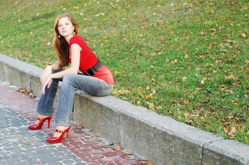 Beautiful woman sit on a road kerb in park. Beautiful woman sit on a road kerb in park