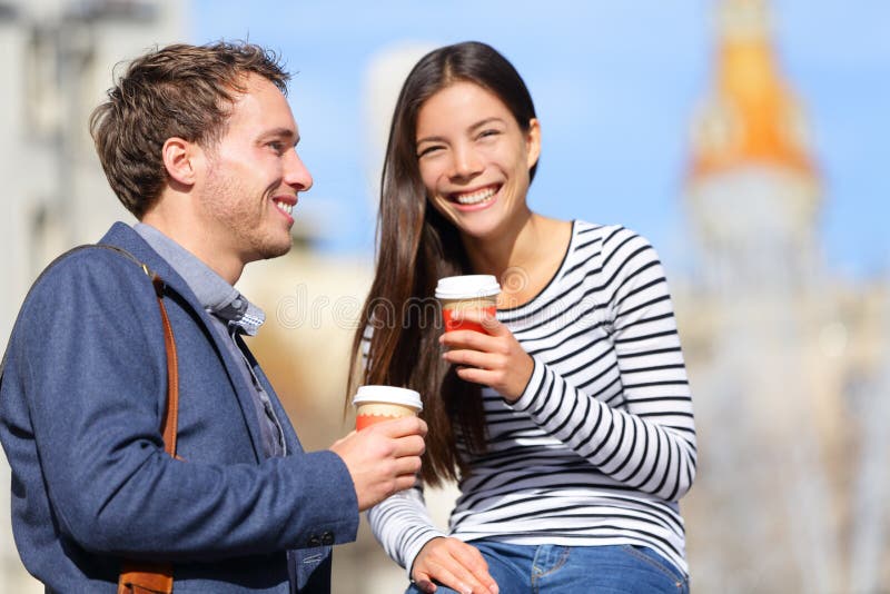 Happy couple drinking coffee talking flirting having fun together. Happy urban young men and women laughing relaxing outside with disposable coffee cup. Caucasian Asian Interracial couple. Happy couple drinking coffee talking flirting having fun together. Happy urban young men and women laughing relaxing outside with disposable coffee cup. Caucasian Asian Interracial couple.