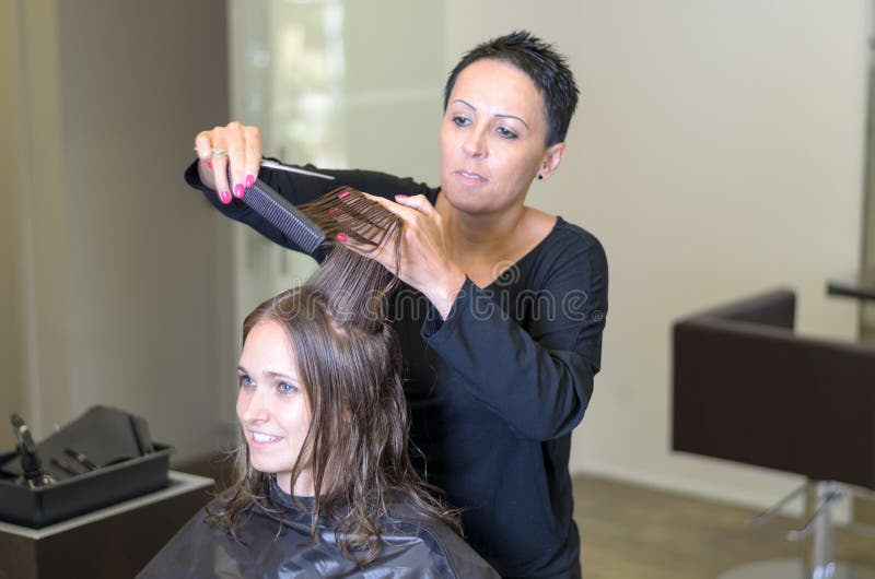 Parrucchiere che sistema i capelli di una giovane donna immagine stock Parrucchiere che sistema i capelli di una giovane donna immagine stock